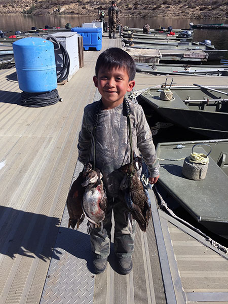 Young hunter displaying waterfowl caught at reservoir lake